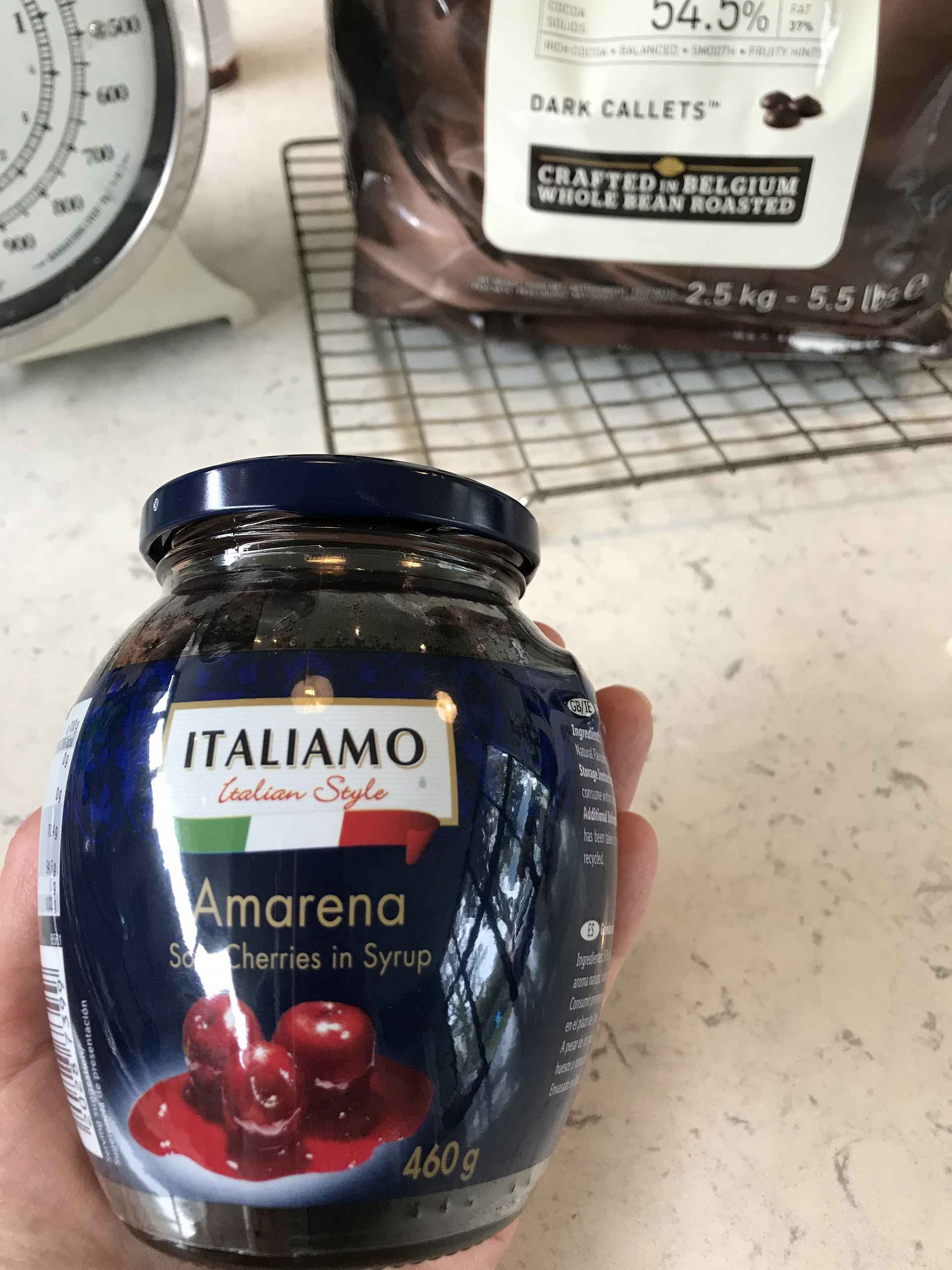 Amarena Cherries in Syrup pot held by someone above a kitchen countertop.
