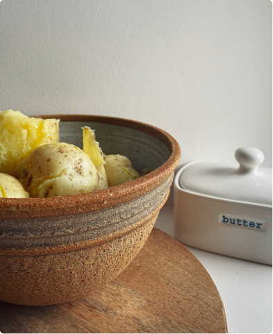 Potatoes in a bowl on a wooden plate with butter on the side.