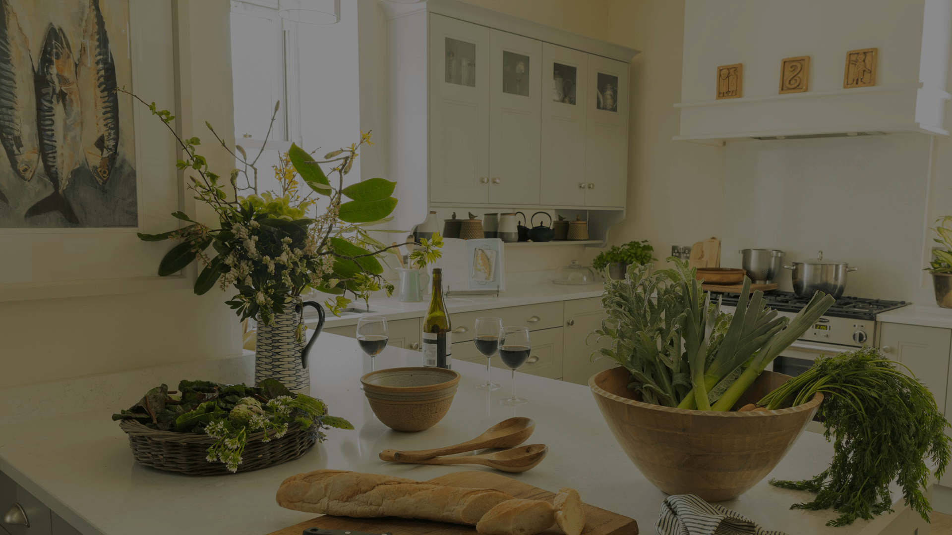 A white kitchen with wine, plants, greens and bred on the table.