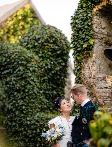 Wedding couple looking at each other with green behind them.