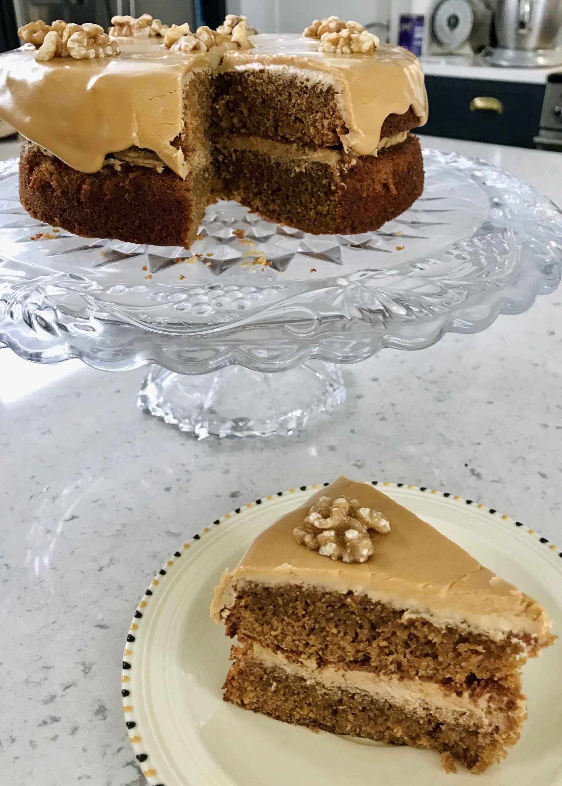 Coffee cake on a glass plate with a slice on a sideplate.