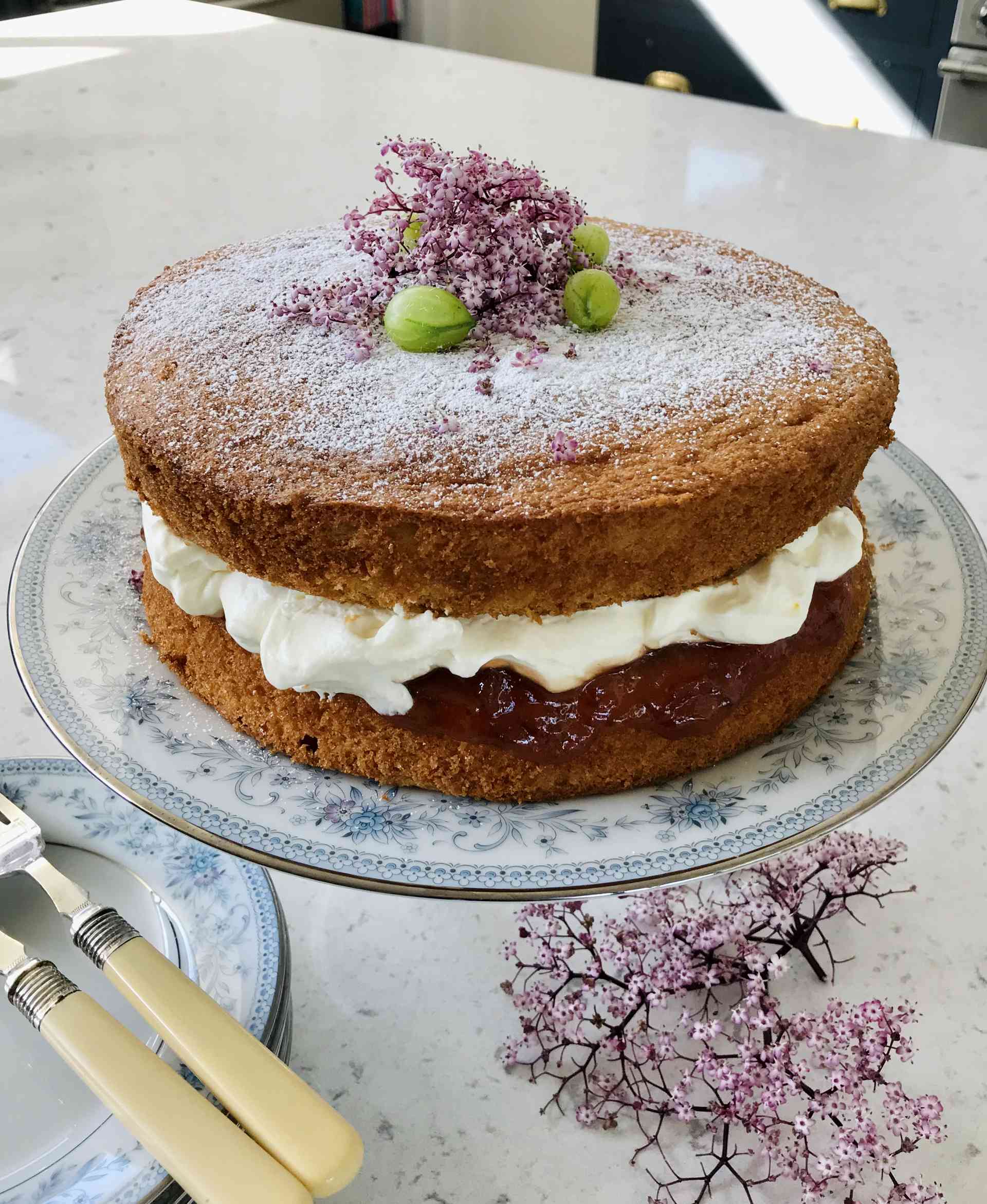 Gooseberry and elderflower chantilly cream sponge cake on a plate on a kitchen countertop.