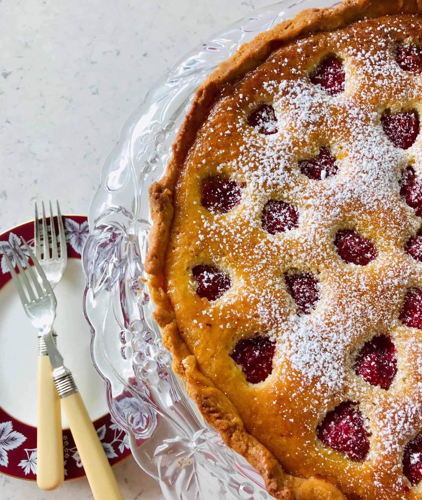 Raspberry frangipane tart with sugar on top on a kitchen countertop.