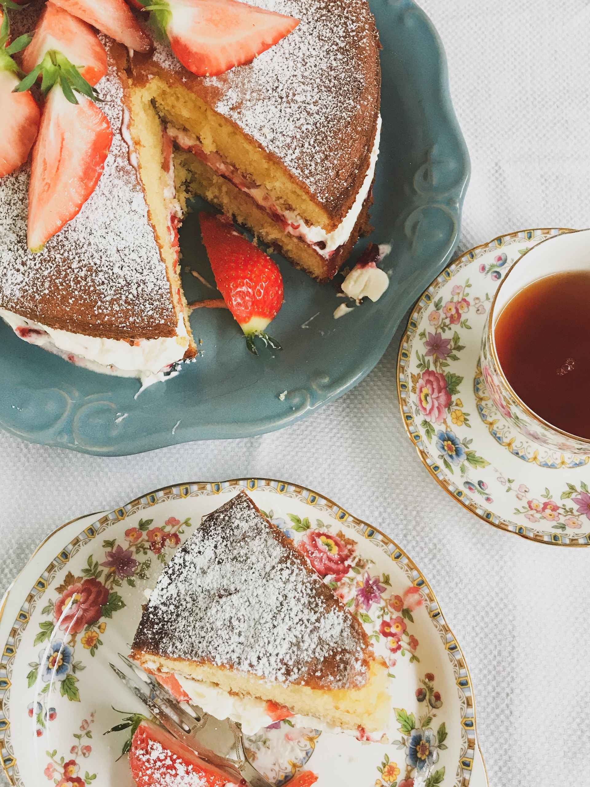 Victoria sponge cake on a plate and a slice on a sideplate with tea.