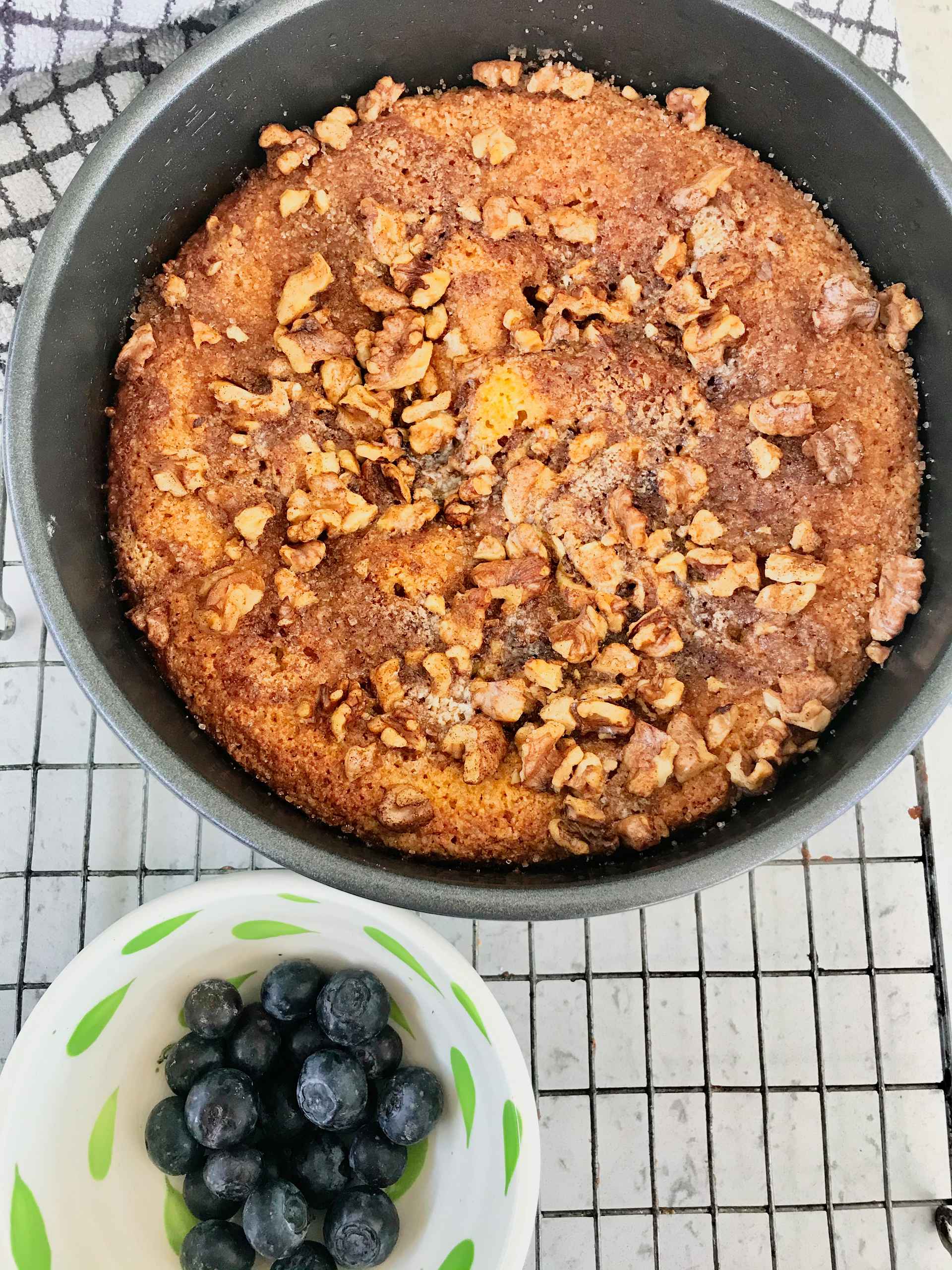 Blueberry Crumble Cake in a cake pan with blueberries on the side in a bowl on a rack.