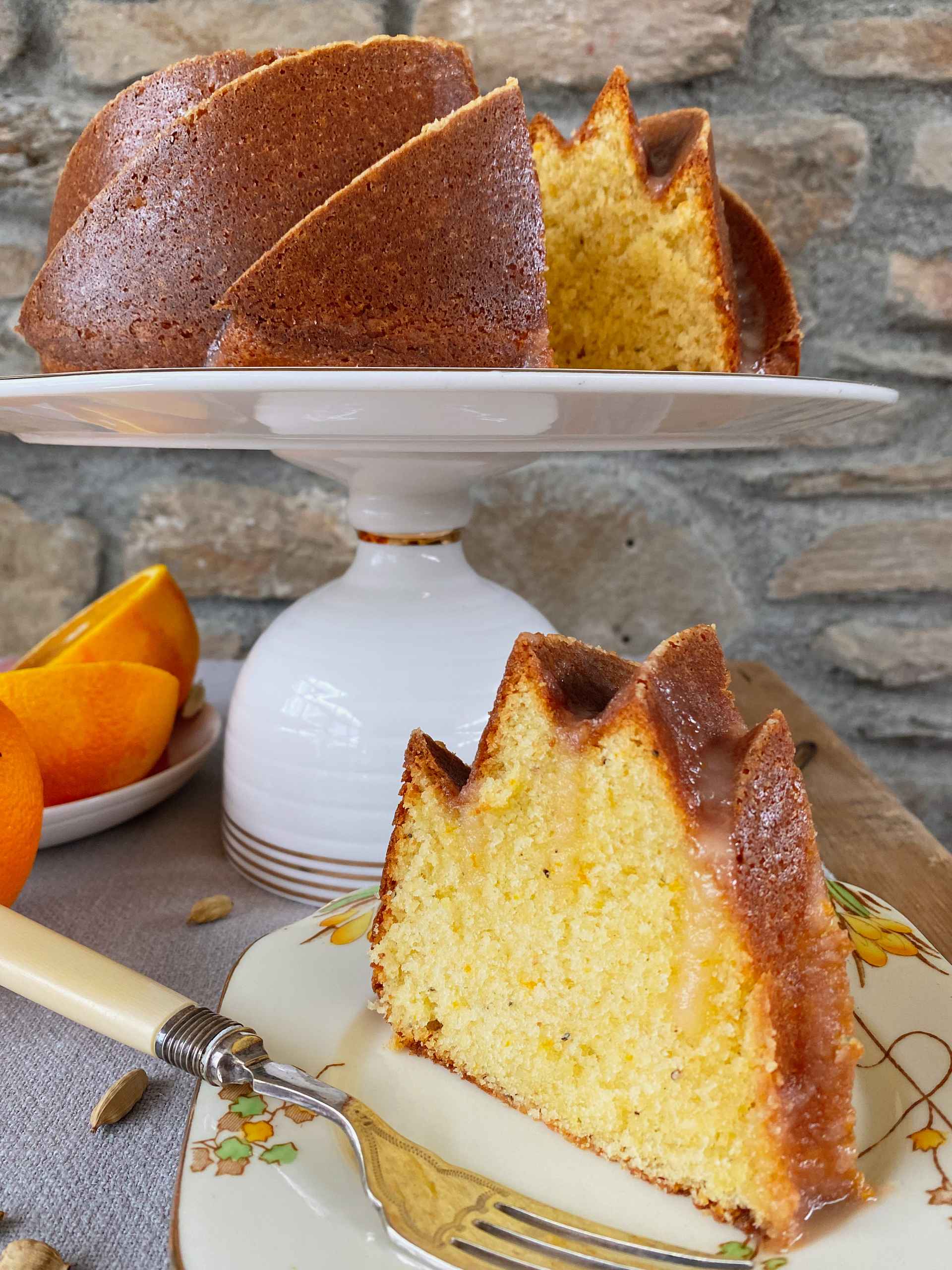 Orange and Cardamon Bundt Cake slice on a sideplate with cake behind.