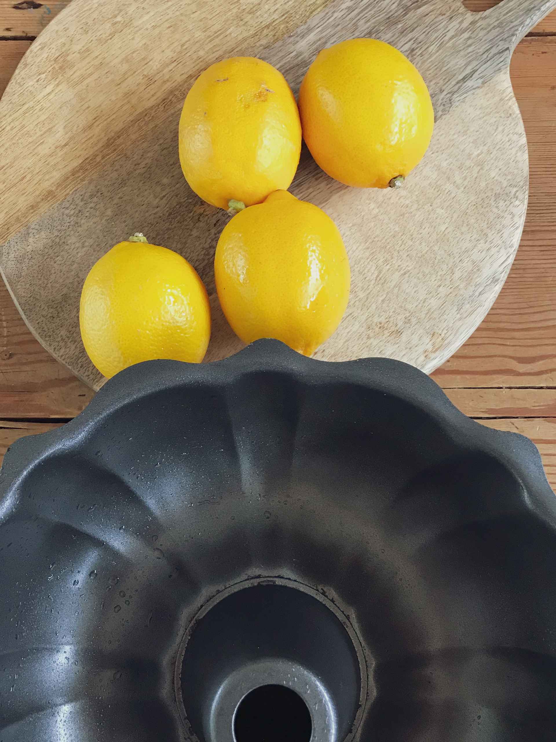 Lemons on a wooden plate next to the cake shape.