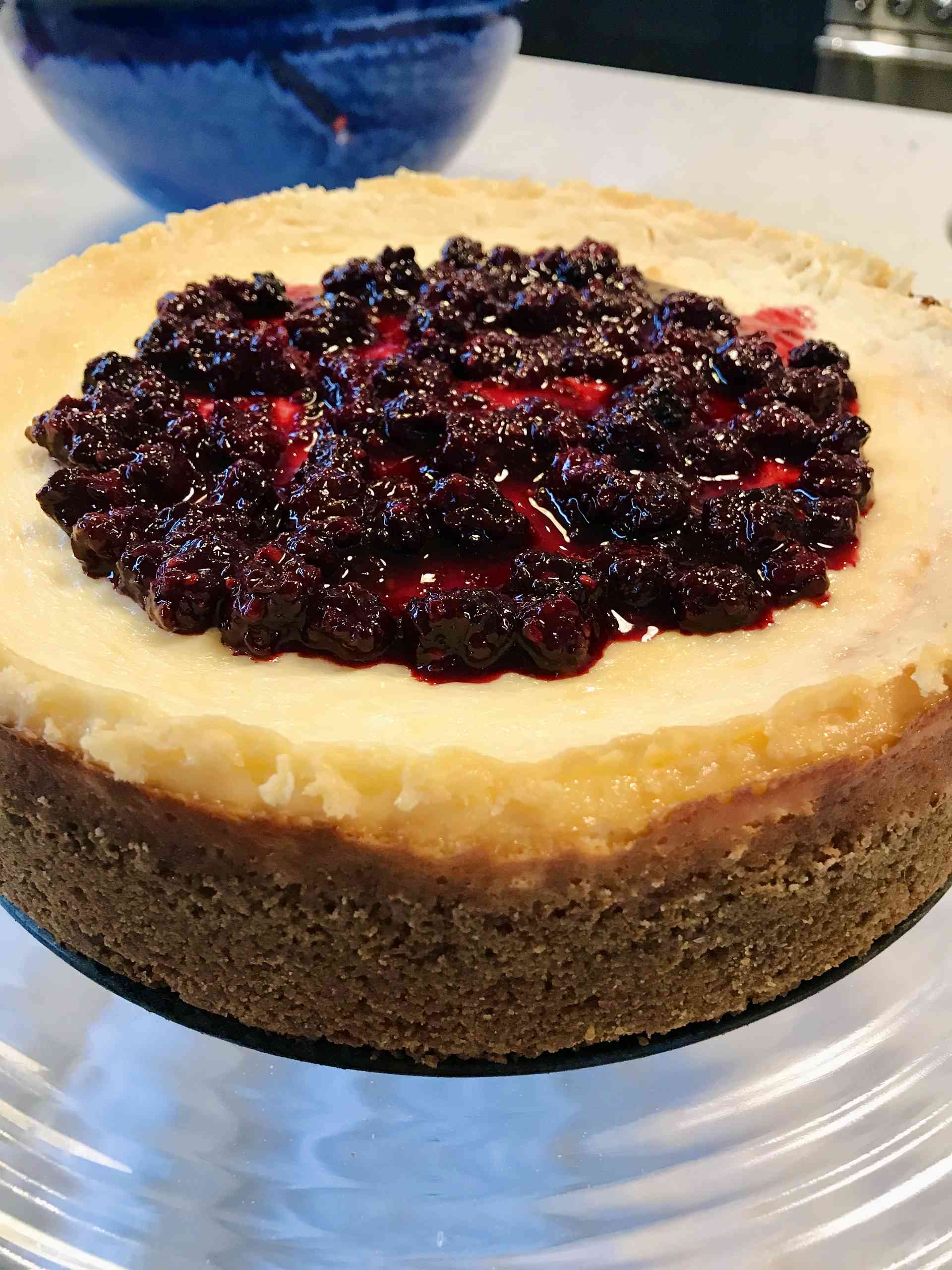 New York cheesecake with blackberry compote on a glass plate.