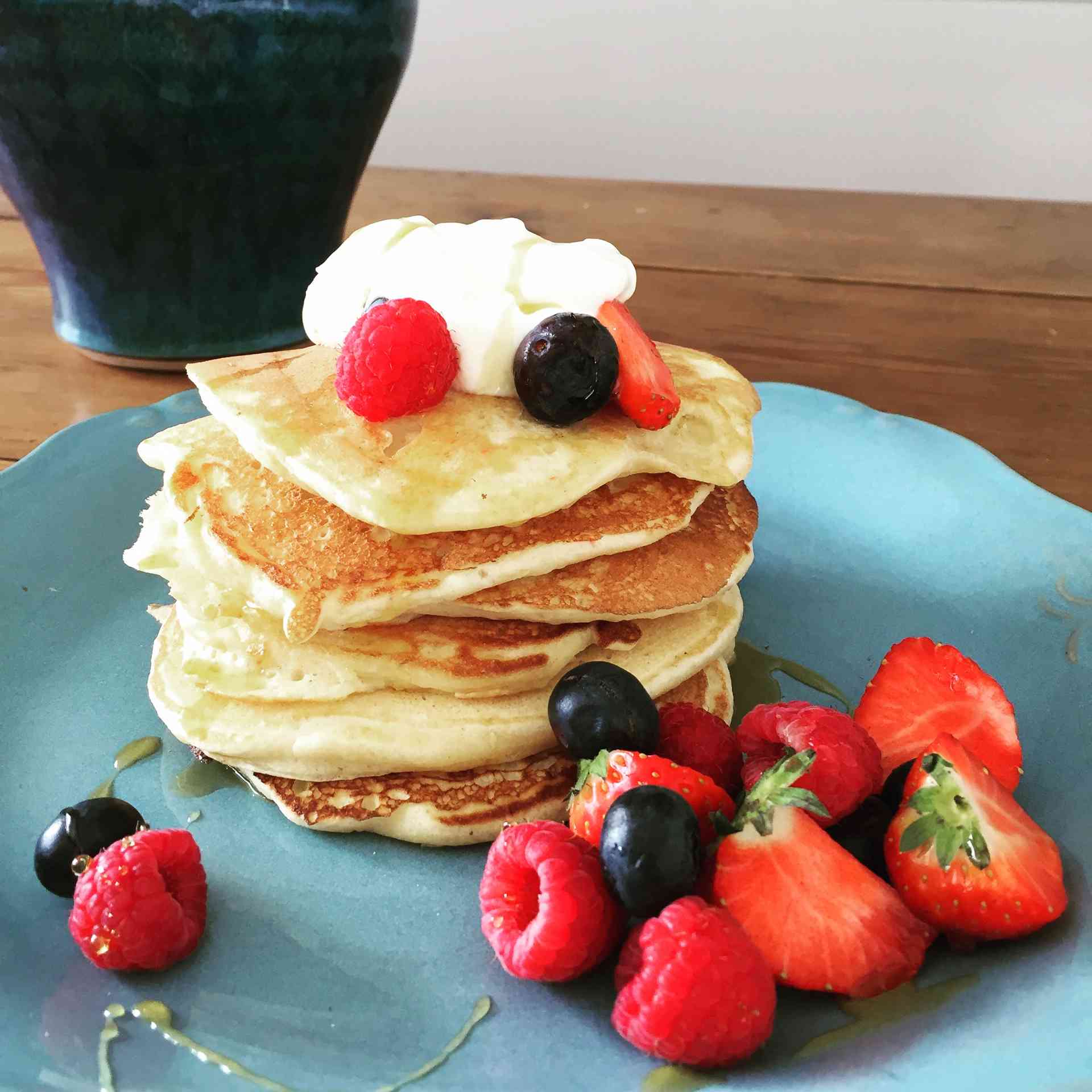 Small pancakes with whipped cream, raspberries, blueberries and strawberries on a plate.
